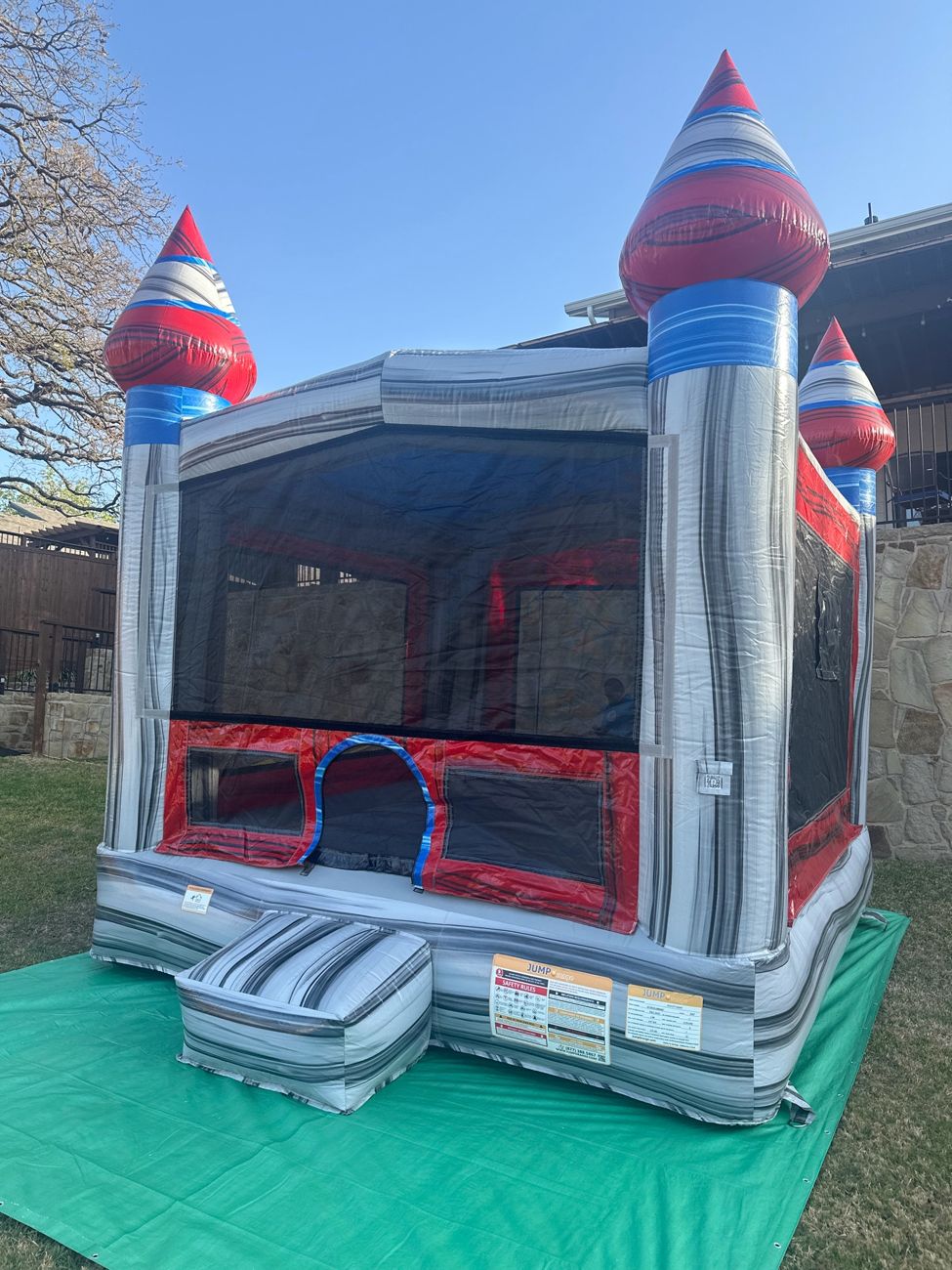 Gray, red and blue castle bounce house set up on a green tarp in a backyard
