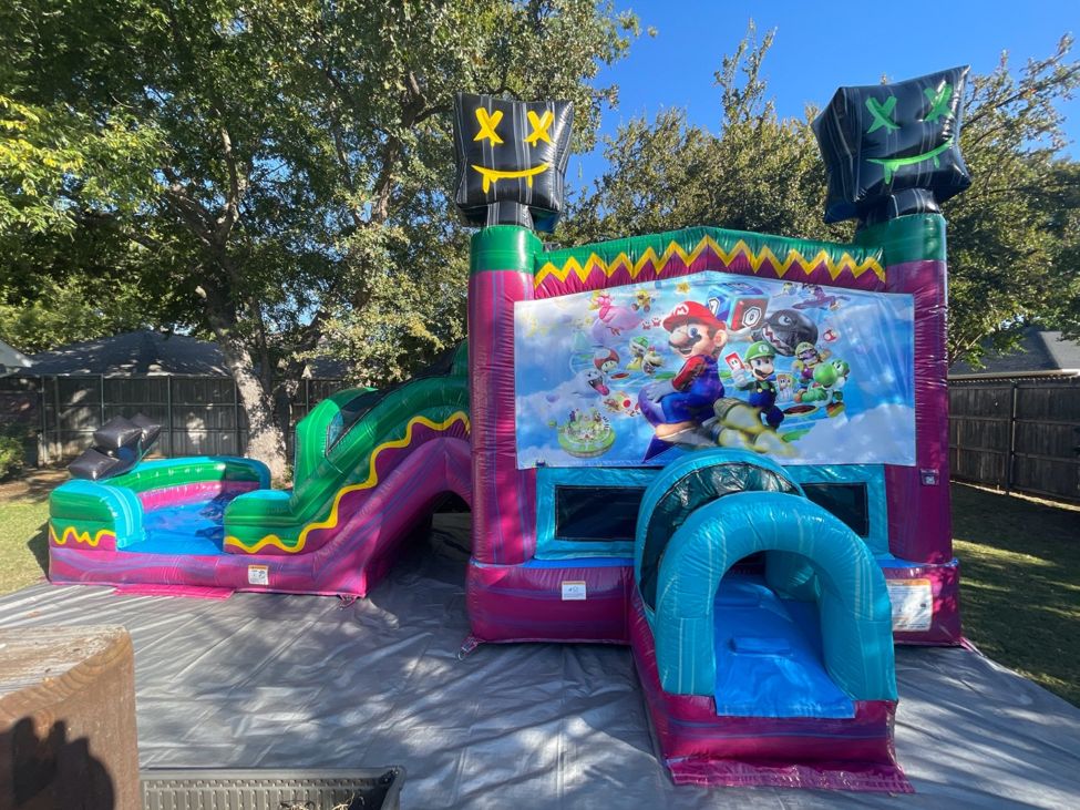 Pink and green combo bounce house with a slide and a character banner, set up on a black tarp in a backyard