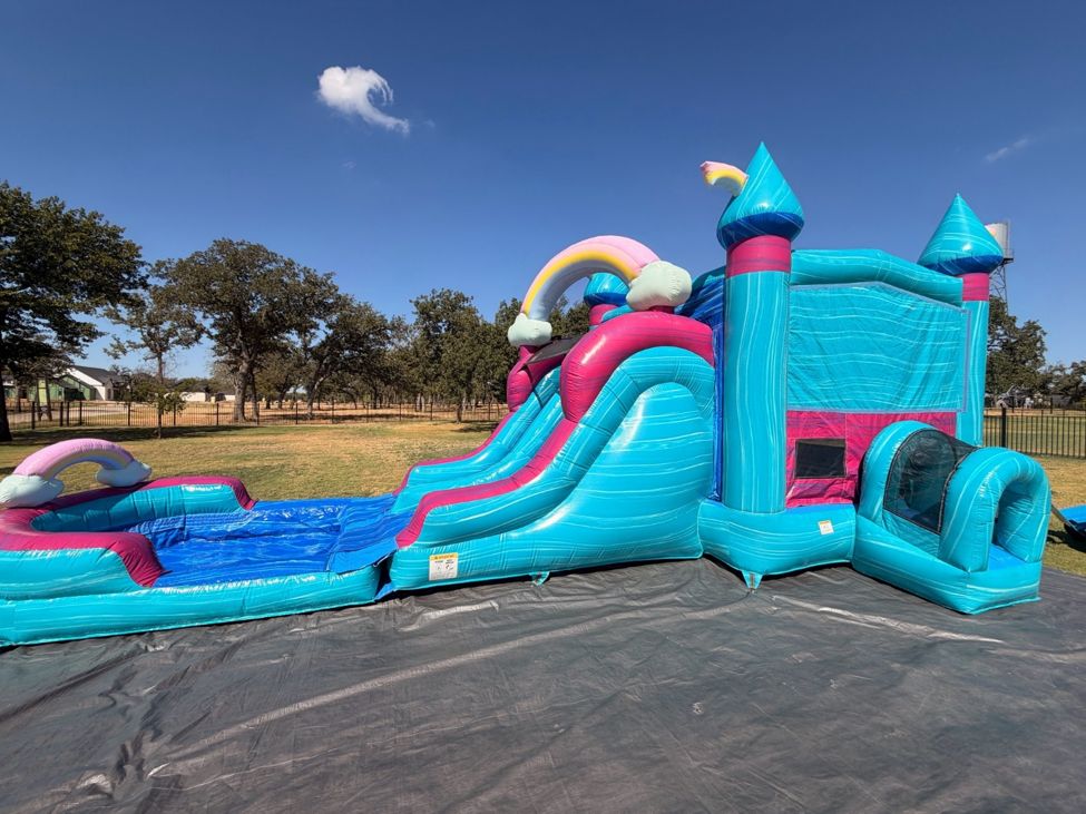Teal and pink bounce house combo with a slide and splash pool set up on a black tarp in an open yard