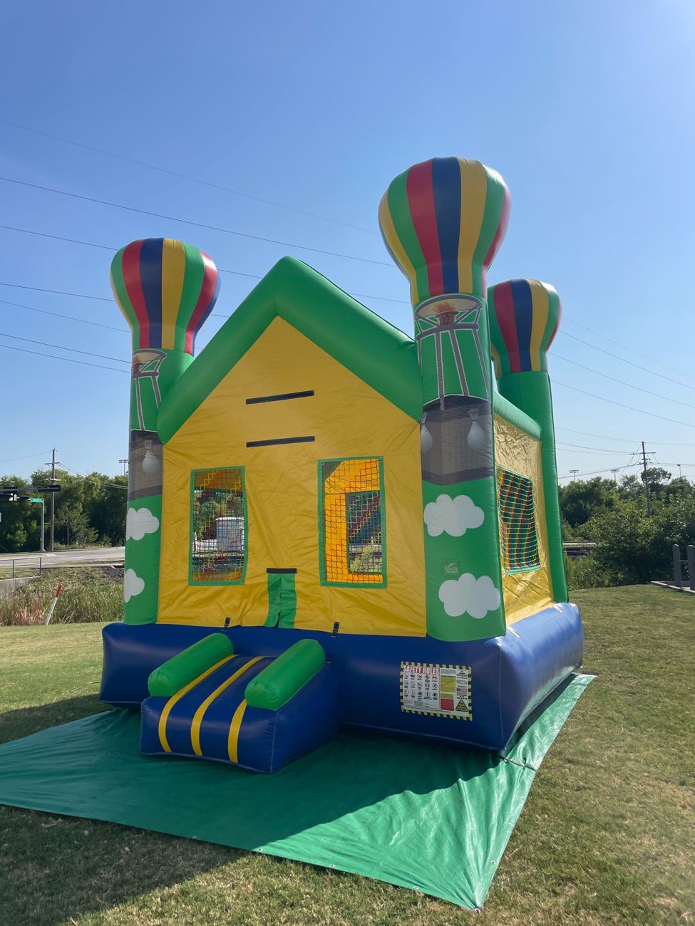 Yellow and green bounce house with striped balloon-style towers and a small slide set up on a green tarp on a lawn