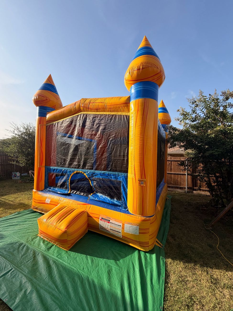 Orange and blue castle bounce house set up on a green tarp in a backyard