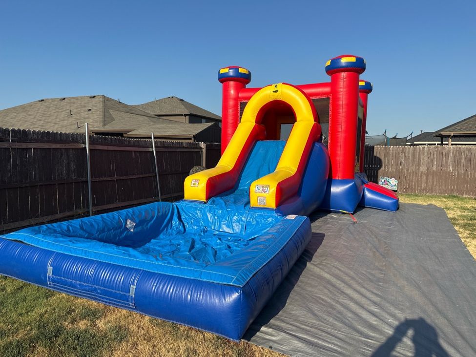 Red, yellow and blue bounce house combo with a slide and a blue splash pool set up on a lawn