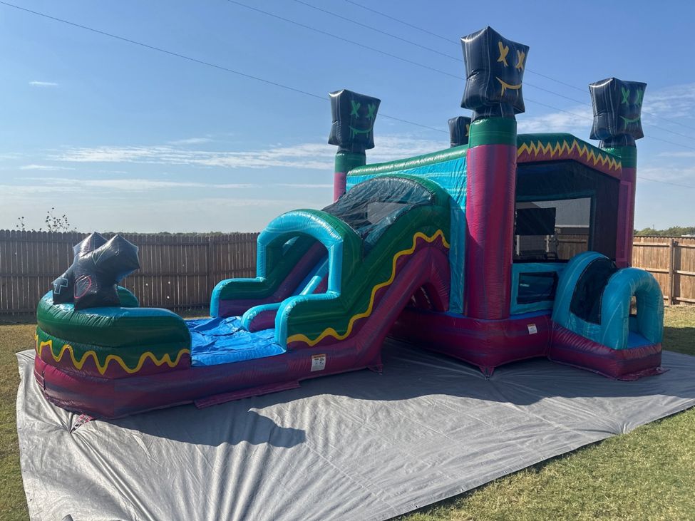 Teal and pink bounce house combo with a slide and splash area set up on a gray tarp on a lawn